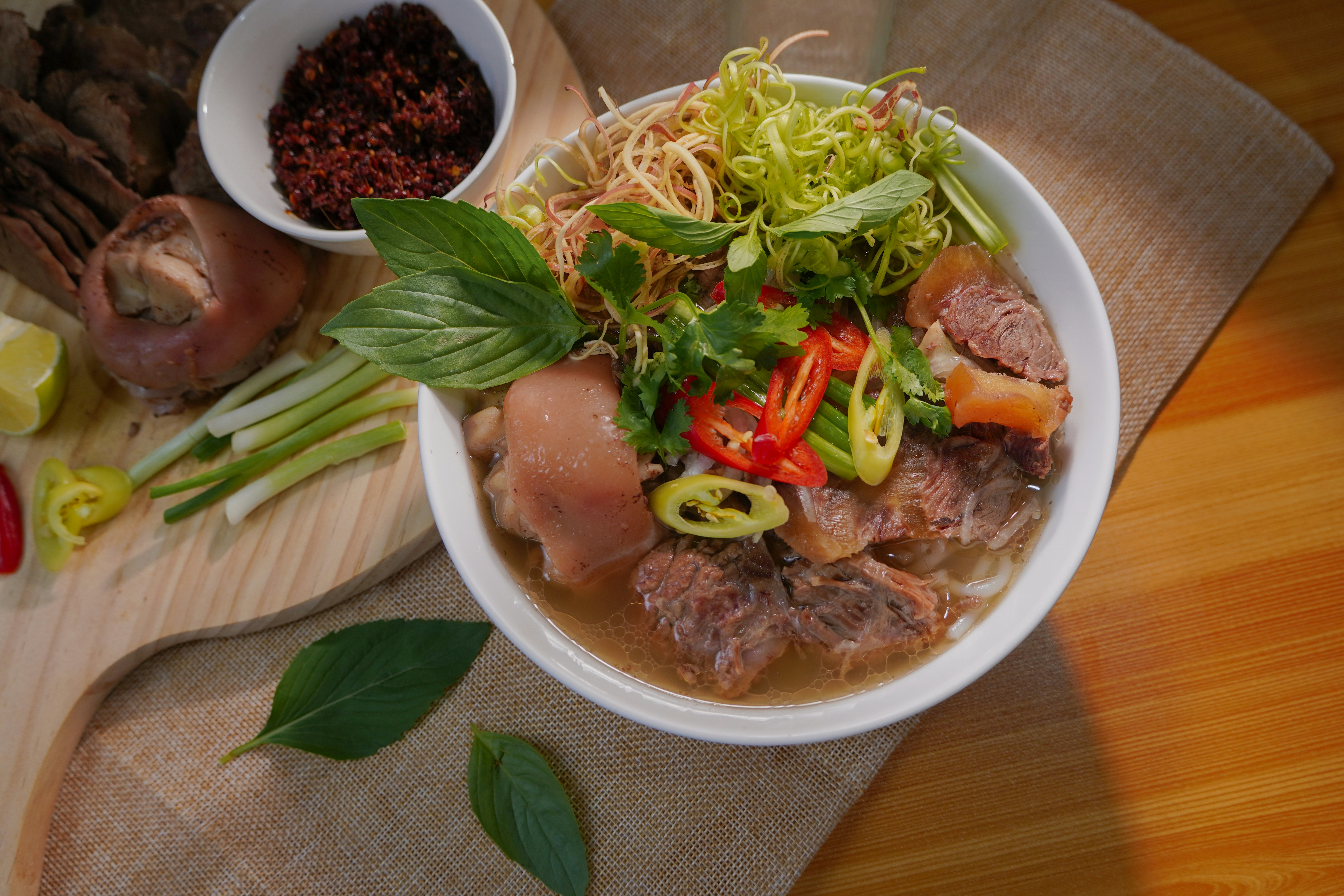 A bowl of Bún Bò Huế with herbs and chilli